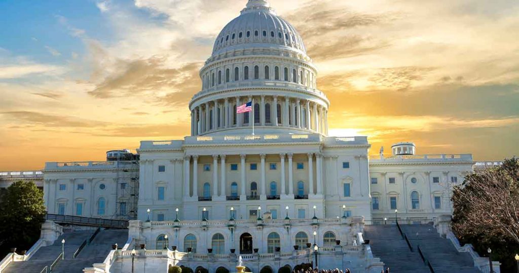 The United States Capitol building with an American flag, lit by a bright sunrise or sunset sky with clouds in the background.